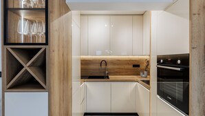 Uma cozinha moderna com armários brancos, bancada de madeira, forno Bosch e espaço para vinhos com copos.