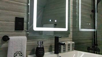 A bathroom with a white sink, a mirror with a light, a towel, and a soap dispenser.