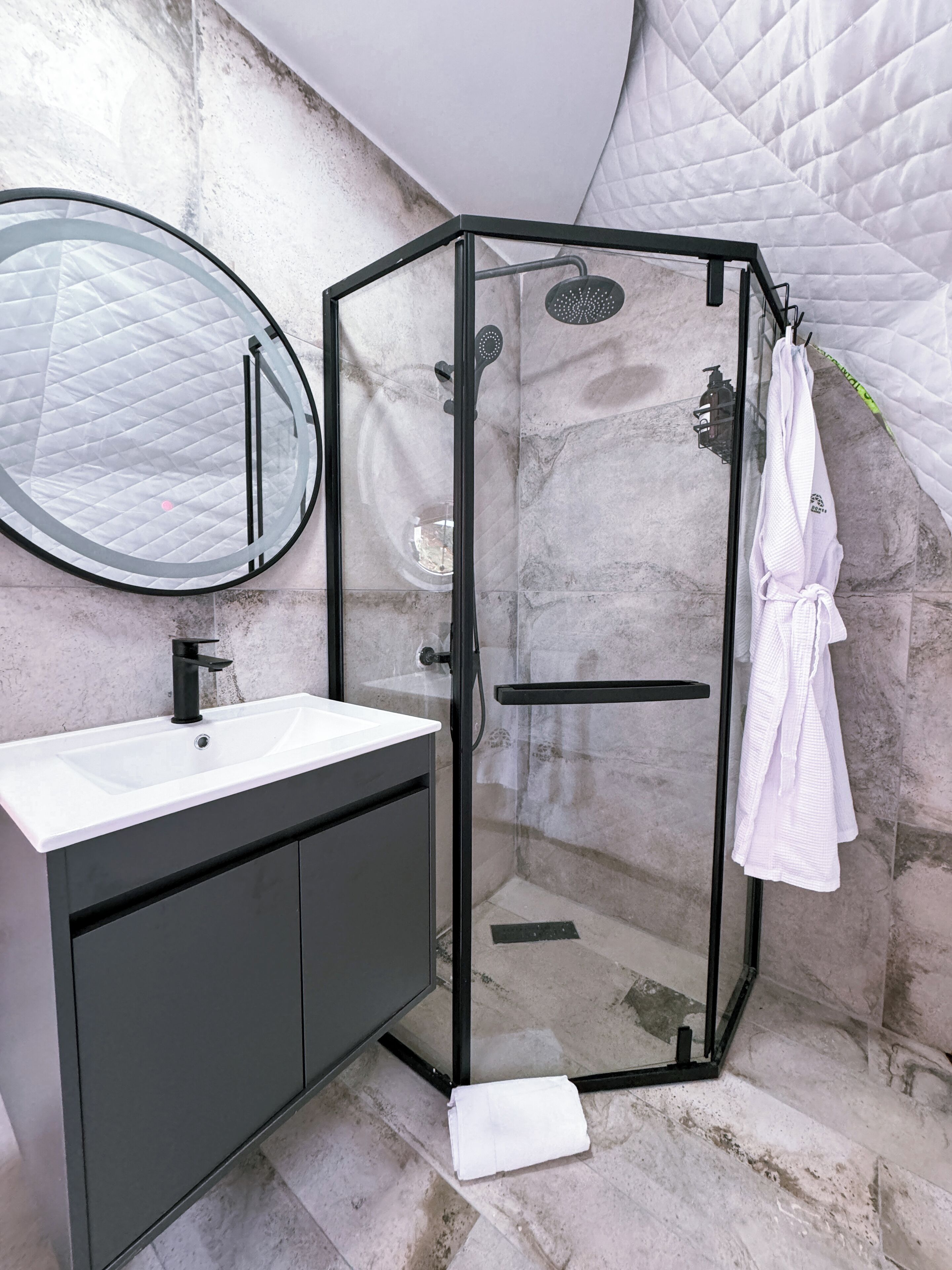 A glass-enclosed shower with a black frame, a white sink with a black faucet, and a mirror above the sink.