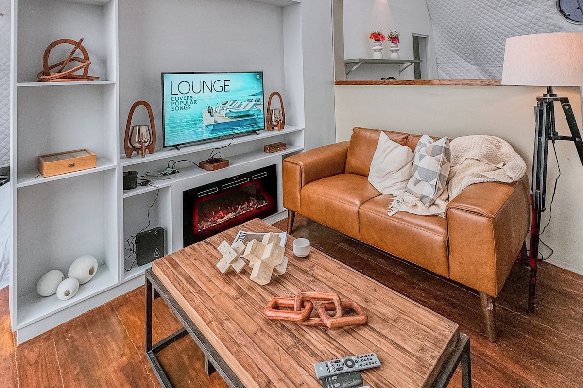 Un salon chaleureux avec un plafond haut, un téléviseur, un canapé en cuir et une table basse en bois.