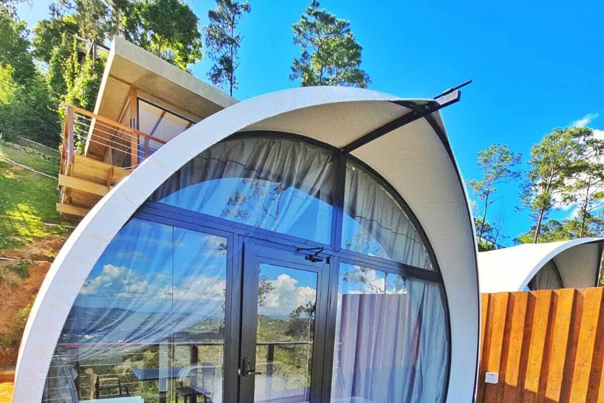 Un espace de vie extérieur moderne, en forme de dôme, doté d’une structure en verre, d’une terrasse en bois et d’une table avec des chaises.
