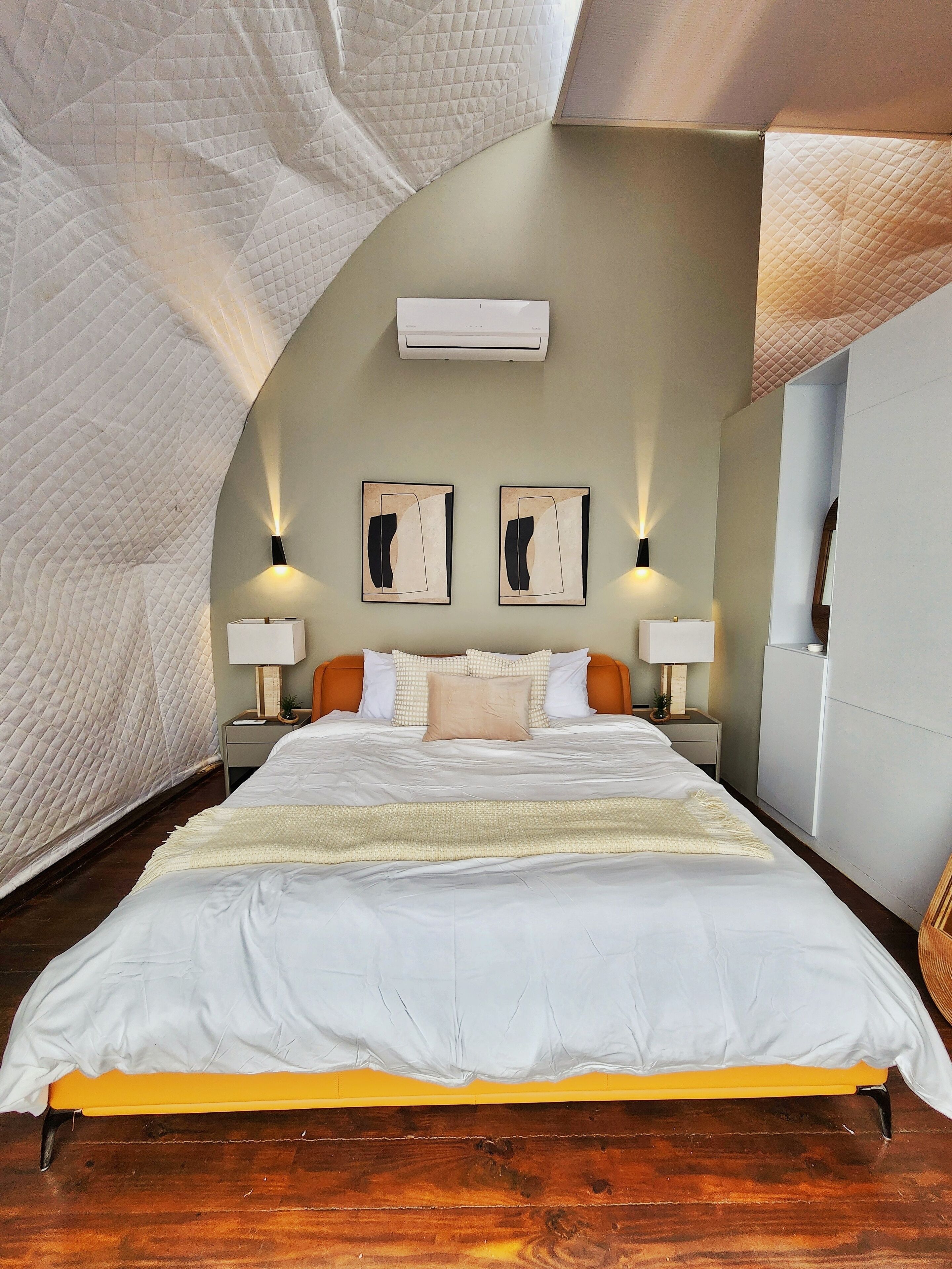 A bedroom with a large bed, two wall-mounted lamps, and two framed artworks.