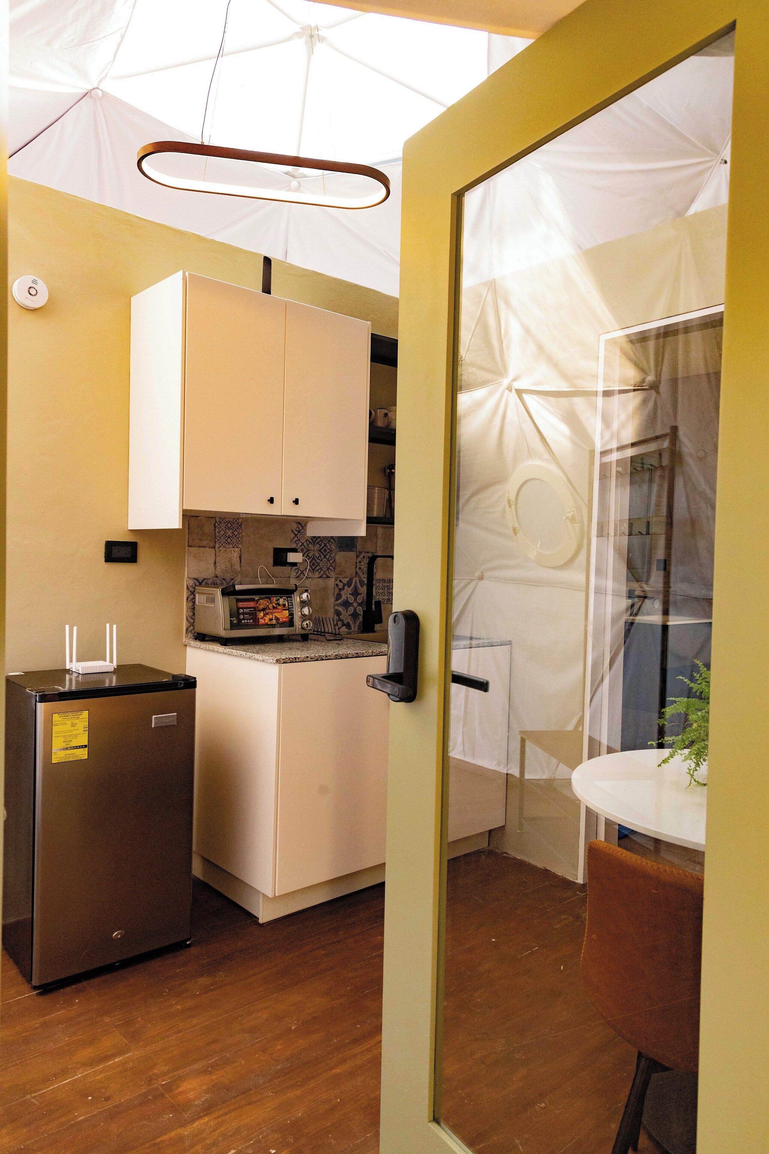 A compact kitchen with a refrigerator, a microwave, and a small oven. There is a dining area with a table and a chair.
