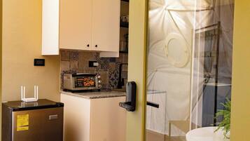 Una cocina compacta con refrigerador, microondas y horno pequeño. Cuenta con un comedor con una mesa y una silla.