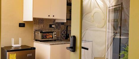 A compact kitchen with a refrigerator, a microwave, and a small oven. There is a dining area with a table and a chair.