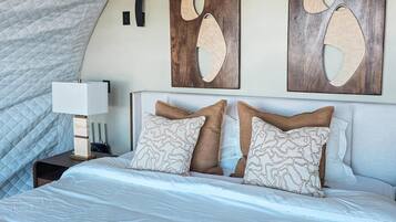 Une chambre à coucher avec un grand lit, une table de chevet, un climatiseur mural et des œuvres d’art abstraites accrochées au mur.