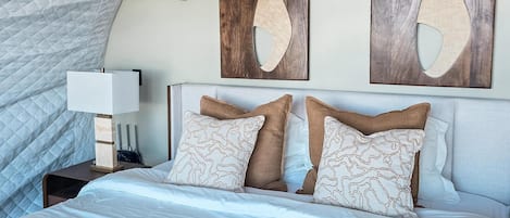 Une chambre à coucher avec un grand lit, une table de chevet, un climatiseur mural et des œuvres d’art abstraites accrochées au mur.