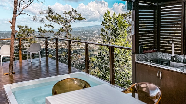 A deck with a pool, chairs, and a table overlooking a cityscape. - The Domes Jarabacoa (Jarabacoa)