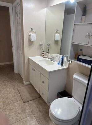 A bathroom with a white sink, mirror, and toilet. There are towels hanging on the wall and a trash bin next to the toilet. - Local quiet stay (Port Charlotte)