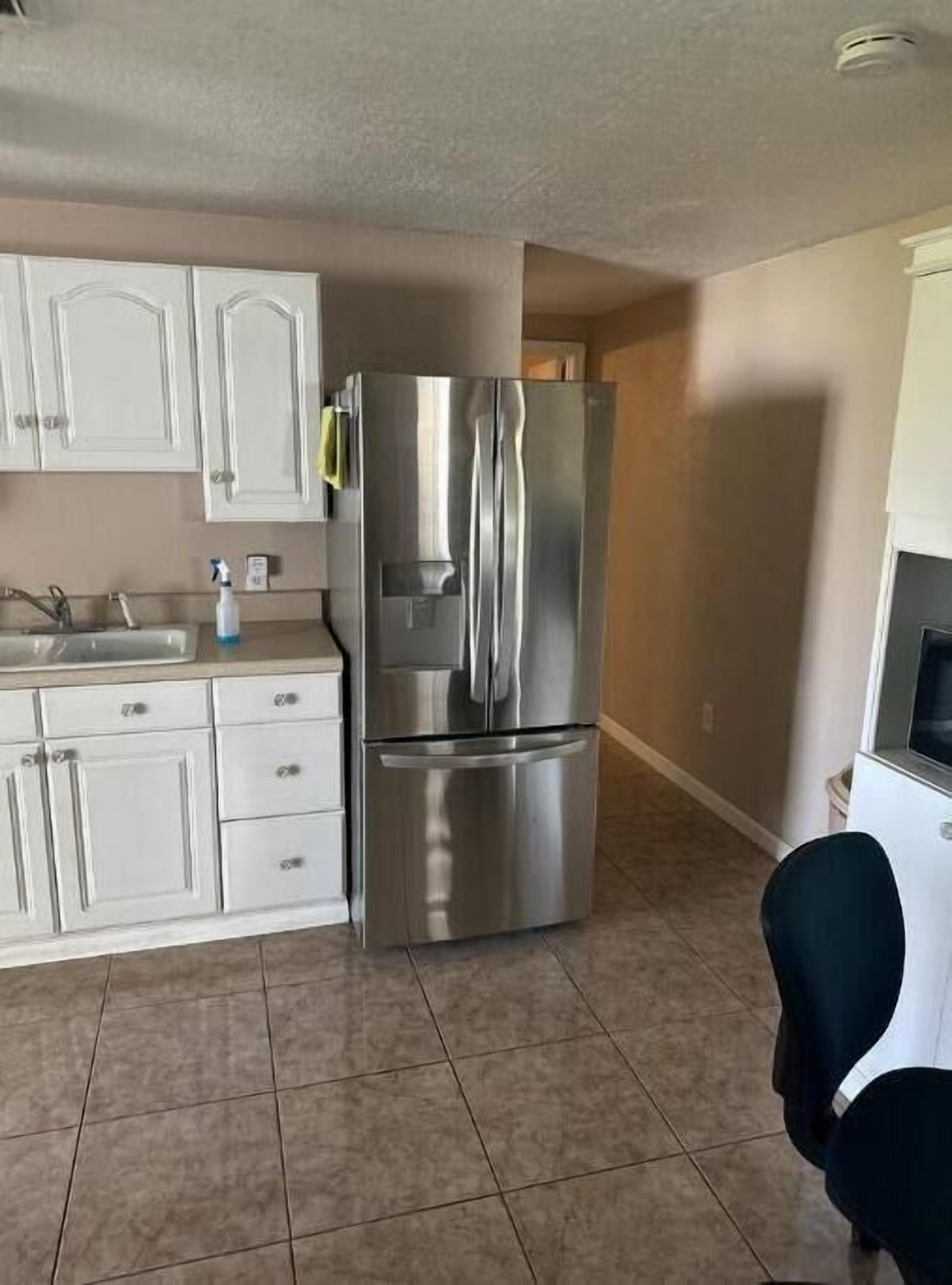 A kitchen with white cabinets, a stainless steel refrigerator, and a tiled floor.