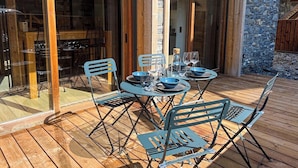 An outdoor dining area with a wooden deck, metal chairs, and a table set for four. - PEARL 001 | LES GETS | Centrer - 4/5 pers. (Les Gets)