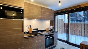 A modern kitchen with a Bosch microwave, a built-in oven, and a large window overlooking a wooden deck. - PEARL 001 | LES GETS | Centrer - 4/5 pers. (Les Gets)