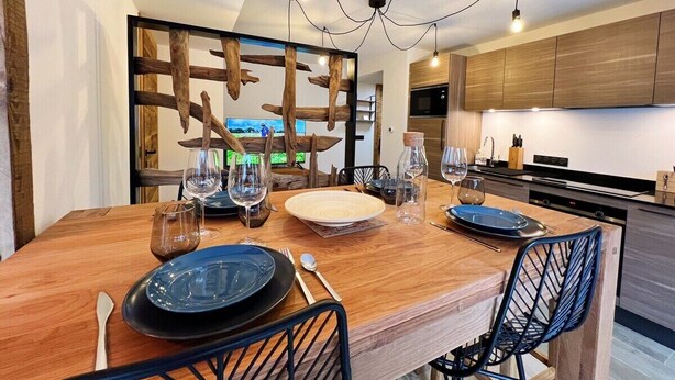 A modern dining area with a wooden table set for four, surrounded by black chairs. - PEARL 001 | LES GETS | Centrer - 4/5 pers. (Les Gets)