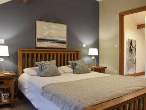 A bedroom with a wooden bed, two bedside tables, a nightstand, a wall-mounted lamp, and a painting above the bed.