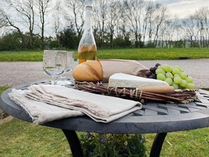 A picnic setup with a bottle, bread, cheese, grapes, and a cloth on a table outdoors.