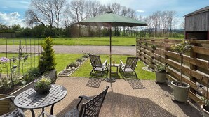 A patio area with a round table and two chairs, a wooden fence, and potted plants. - Pippa's Cottage - UK42332 (Greystoke, near Penrith)