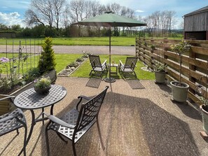 A patio area with a round table and two chairs, a wooden fence, and potted plants.