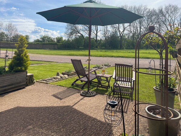 A patio with two wooden chairs, a table, a green umbrella, and a potted plant.