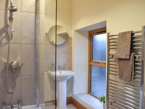 A bathroom with a glass shower enclosure, a pedestal sink, a round mirror, a towel rack, and a window.