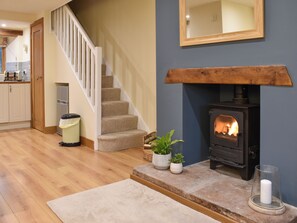 A cozy living room with a fireplace, a staircase, and a kitchen area. - Pippa's Cottage - UK42332 (Greystoke, near Penrith)