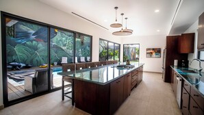 Una cocina moderna con una isla grande, armarios de madera y vistas a una piscina a través de amplios ventanales.