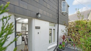 Ein modernes Haus mit weißer Fassade, einer sichtbaren Küche und einem kleinen Gartenbereich mit Blumentöpfen.