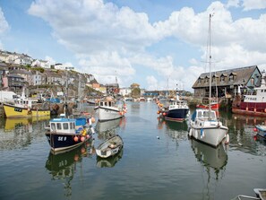 Un port où sont amarrés divers bateaux, un bâtiment portant une enseigne « FY848 », et des maisons le long du quai.