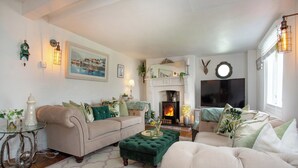 Ein gemütliches Wohnzimmer mit Kamin, einer Couch, einem grünen Hocker und einem Fernseher.