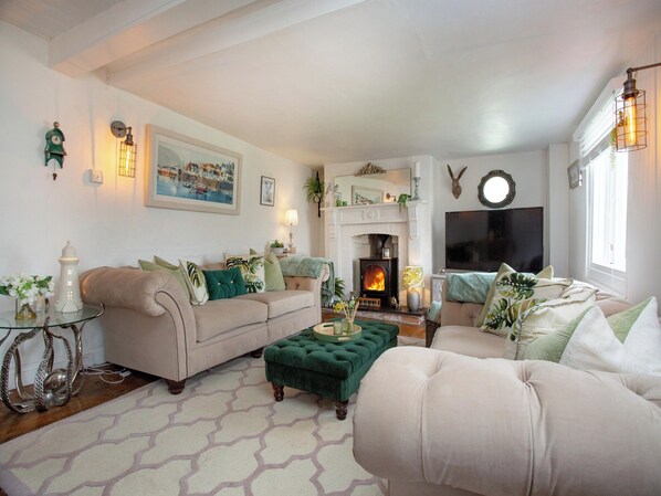 Una sala de estar acogedora con chimenea, un sofá, un reposapiés verde y un televisor.