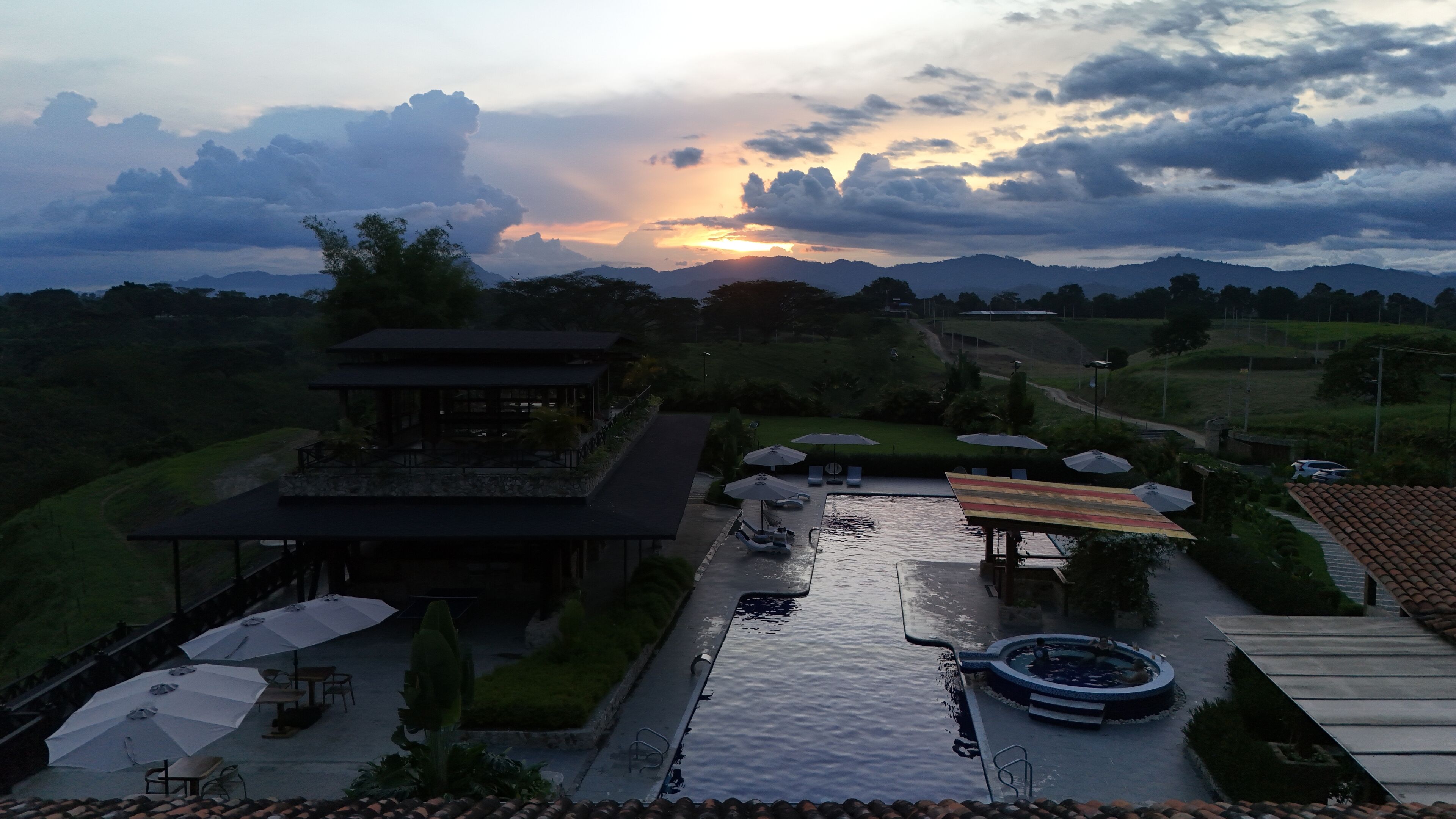 Un resort con piscina, sombrillas y vistas al atardecer sobre montañas.