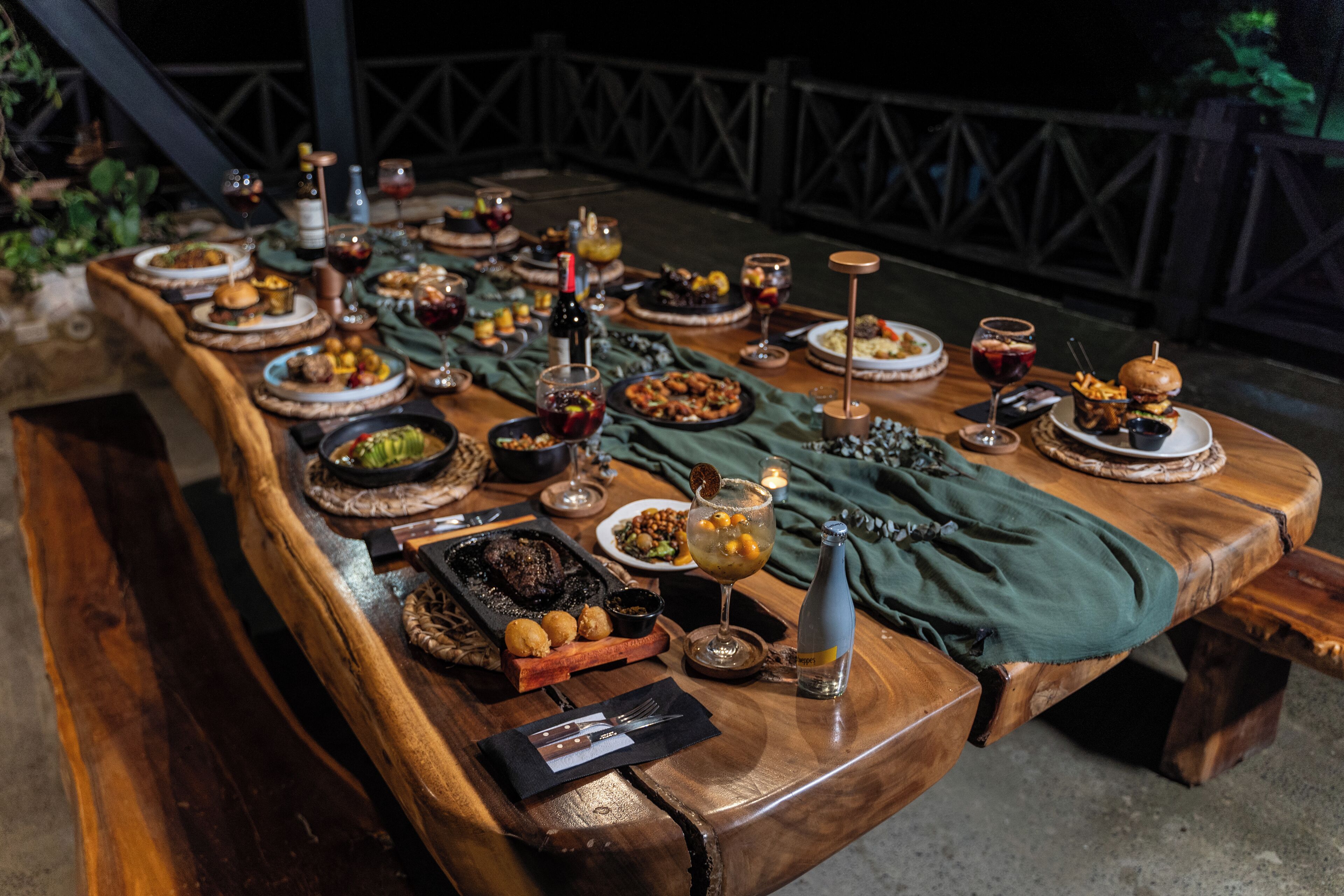 A long wooden table set with various dishes, drinks, and candles, suggesting a formal dining setup.