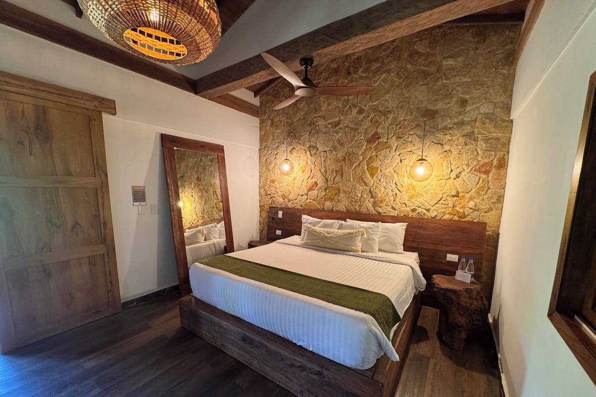 Une chambre avec un mur en pierre, un cadre de lit en bois et un ventilateur de plafond.