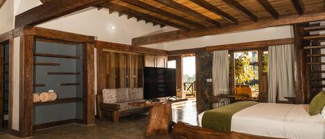 A spacious room with a large bed, wooden furniture, a television, and a stone wall.