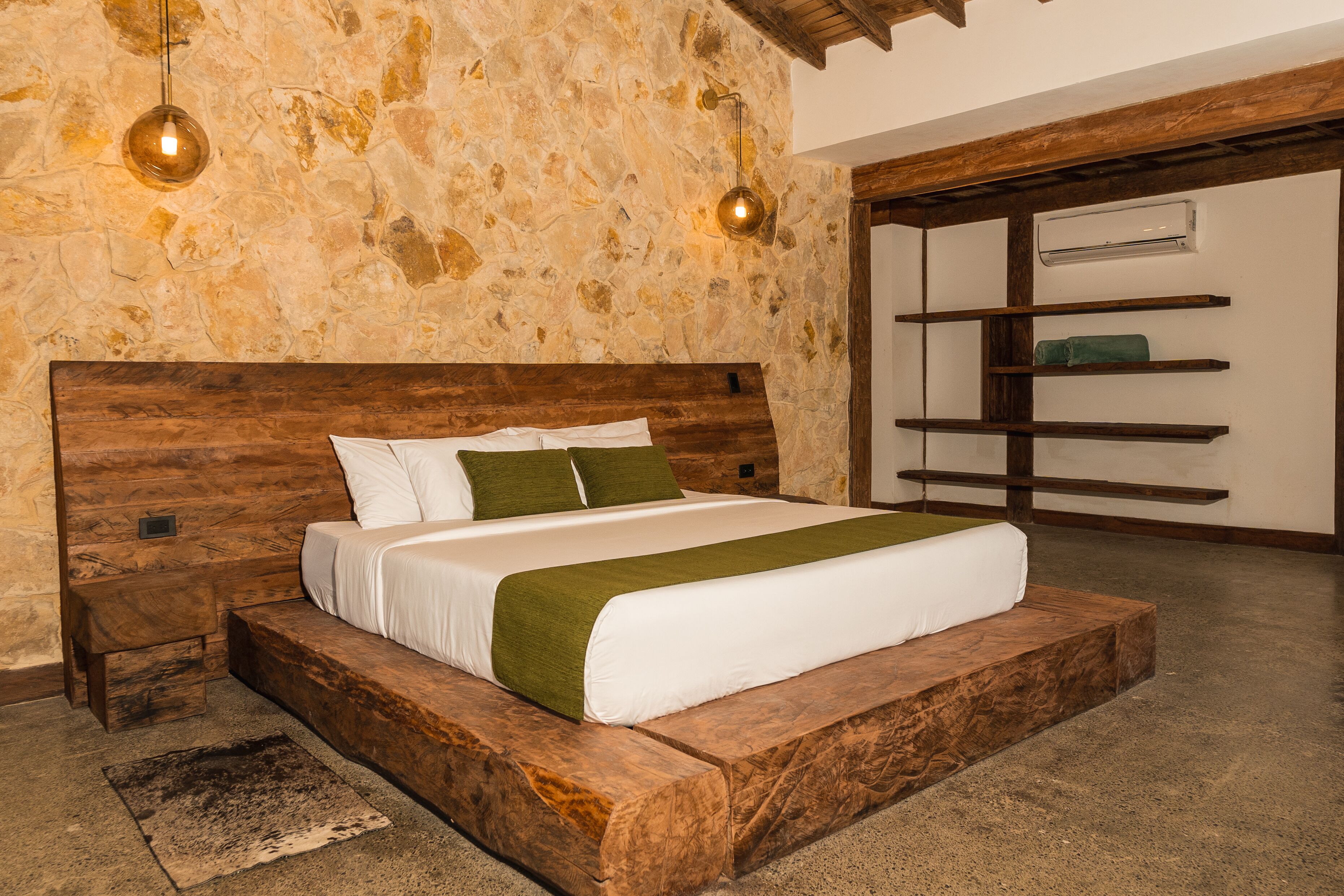 Un dormitorio con pared de piedra, cabecera de madera y estanterías empotradas.