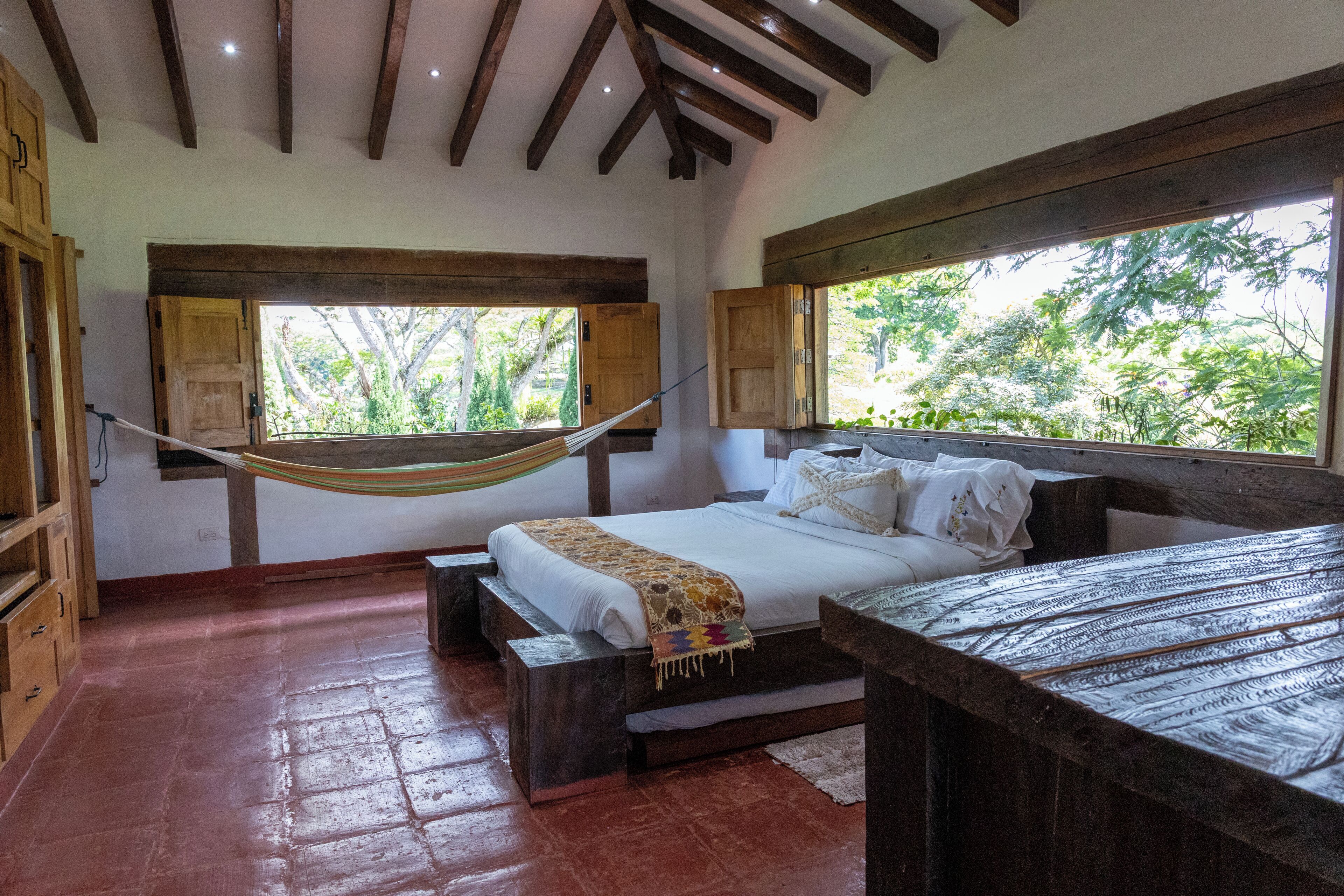 A bedroom with a bed, wooden headboard, windows, and a hammock.