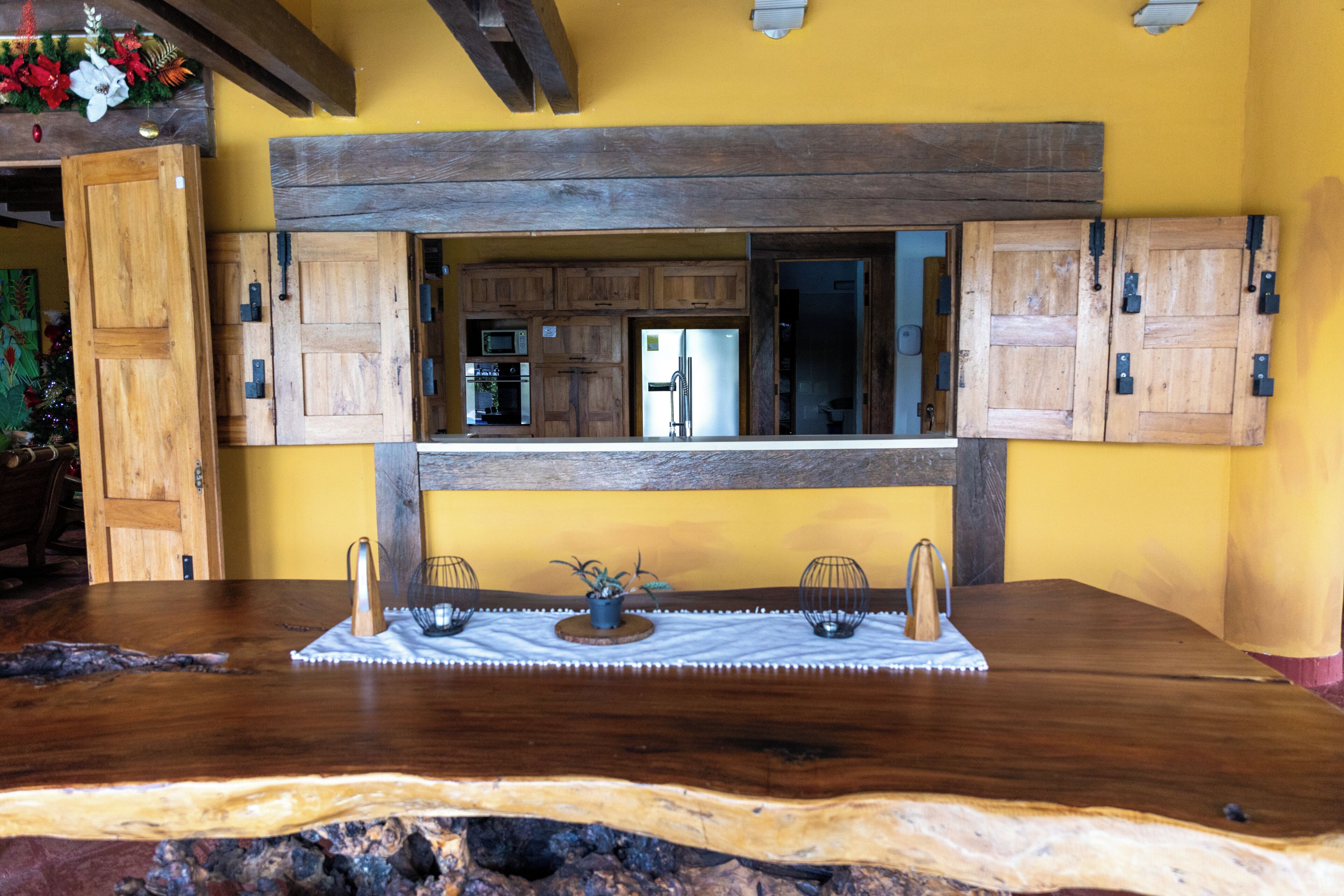 A wooden dining table with a rustic finish, a built-in kitchen area with wooden cabinets, and a decorative plant centerpiece.