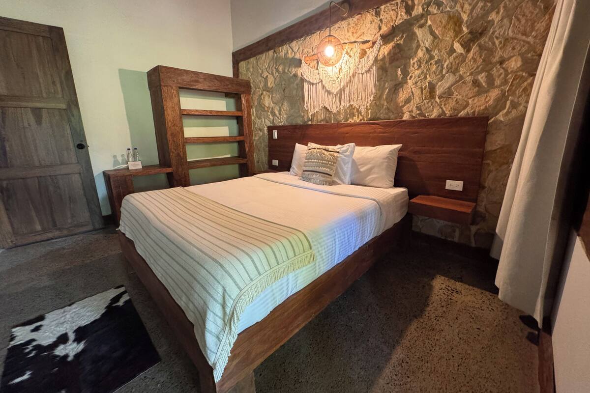 Un lit avec une tête de lit en bois, un mur en pierre et une table de chevet avec une lampe.