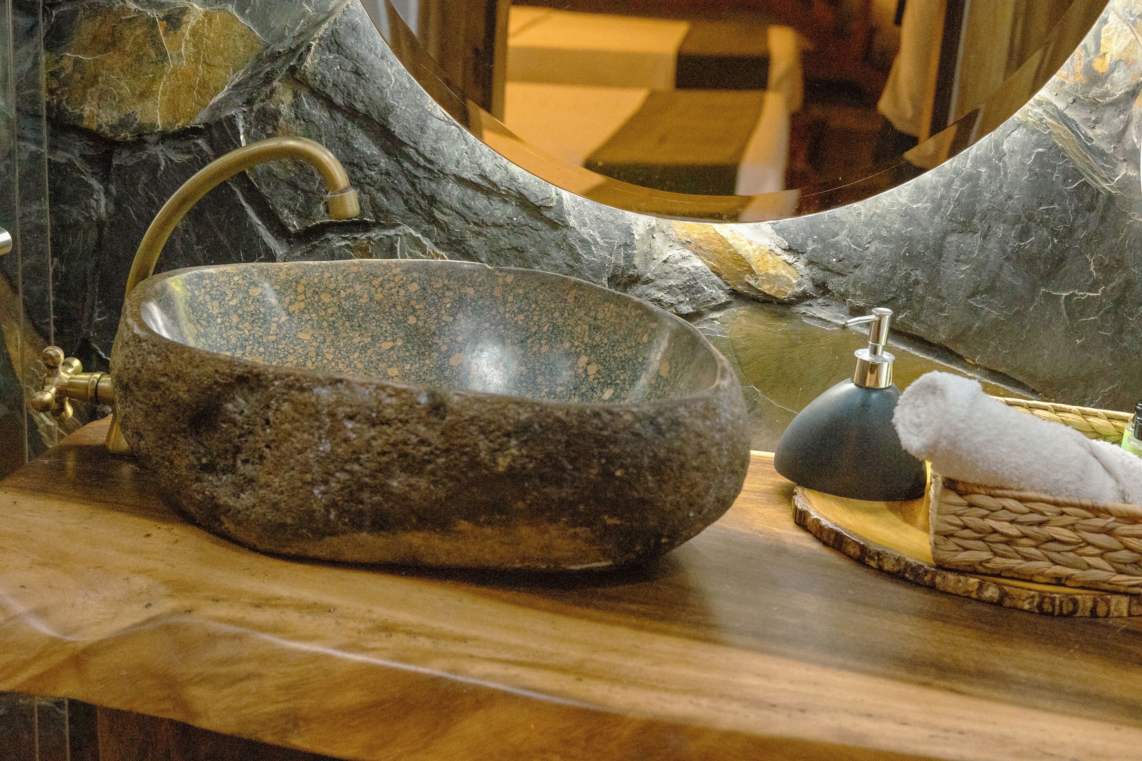A stone sink with a faucet, a soap dispenser, and a towel on a wooden surface.