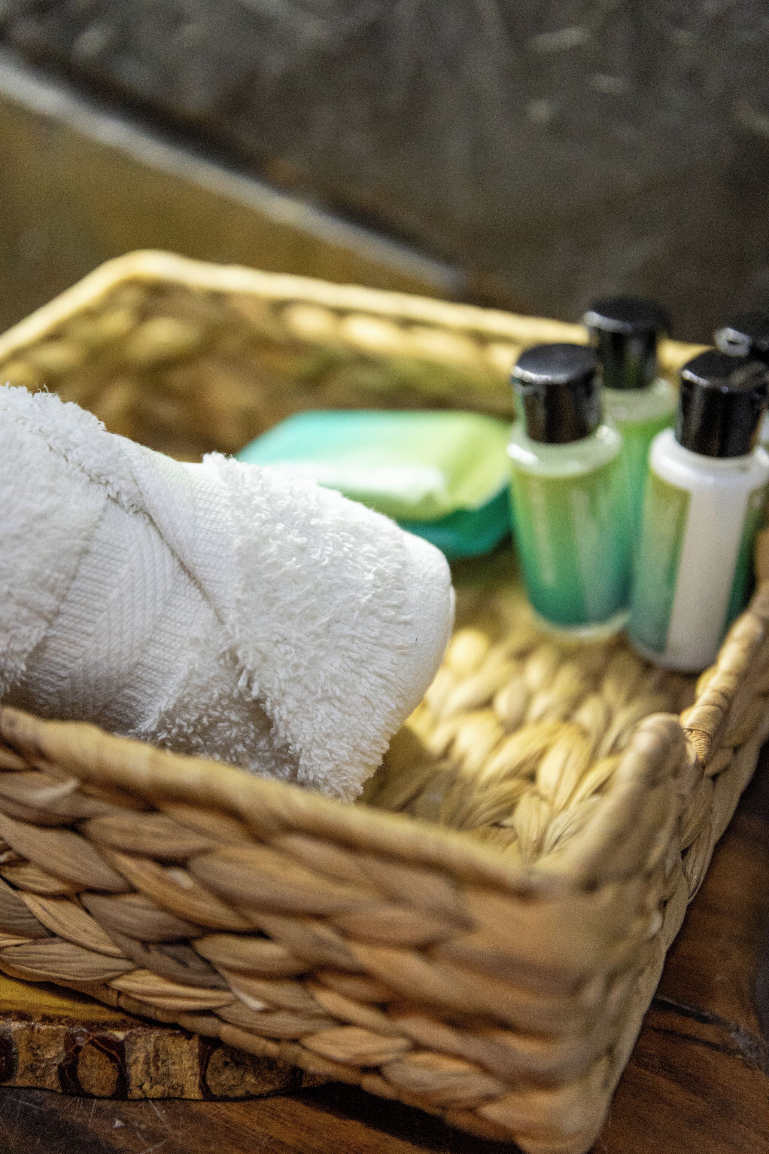 A woven basket containing a white towel and three bottles of green and white liquid.