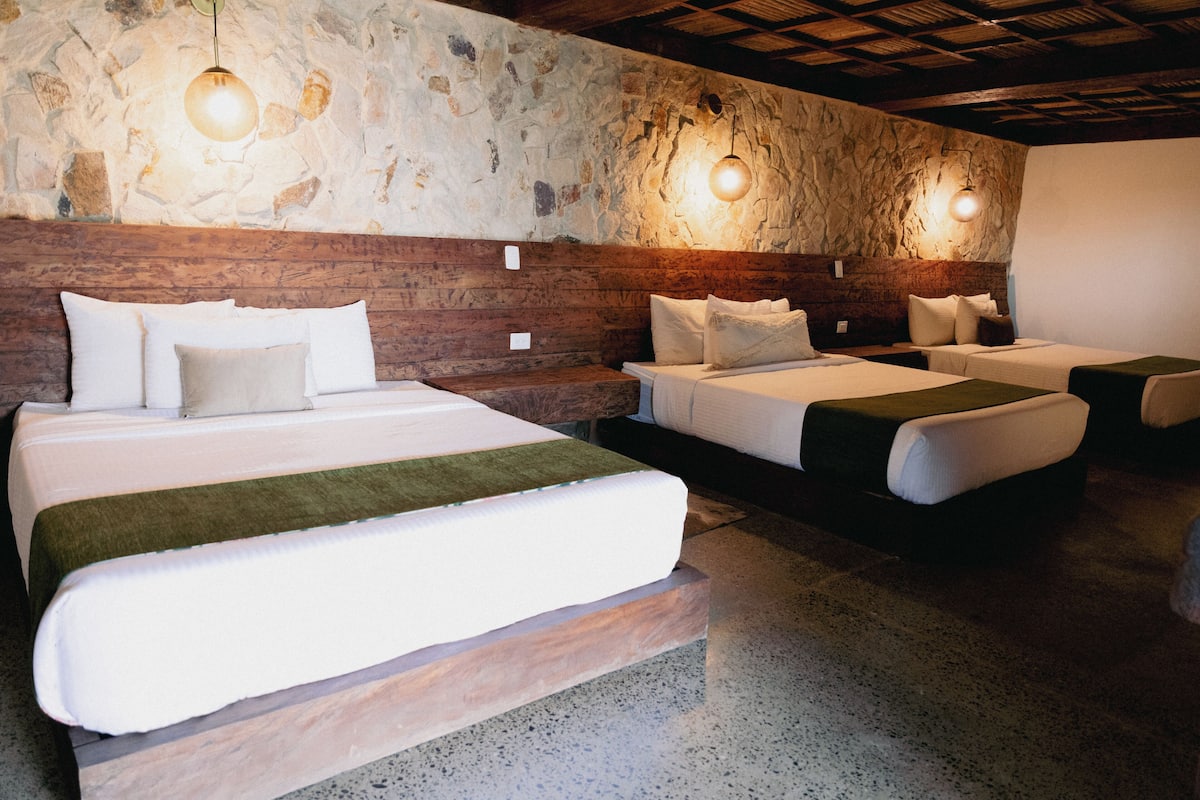 Une chambre d’hôtel avec un mur en pierre, une tête de lit en bois et deux lits avec une literie blanche et des plaids verts.