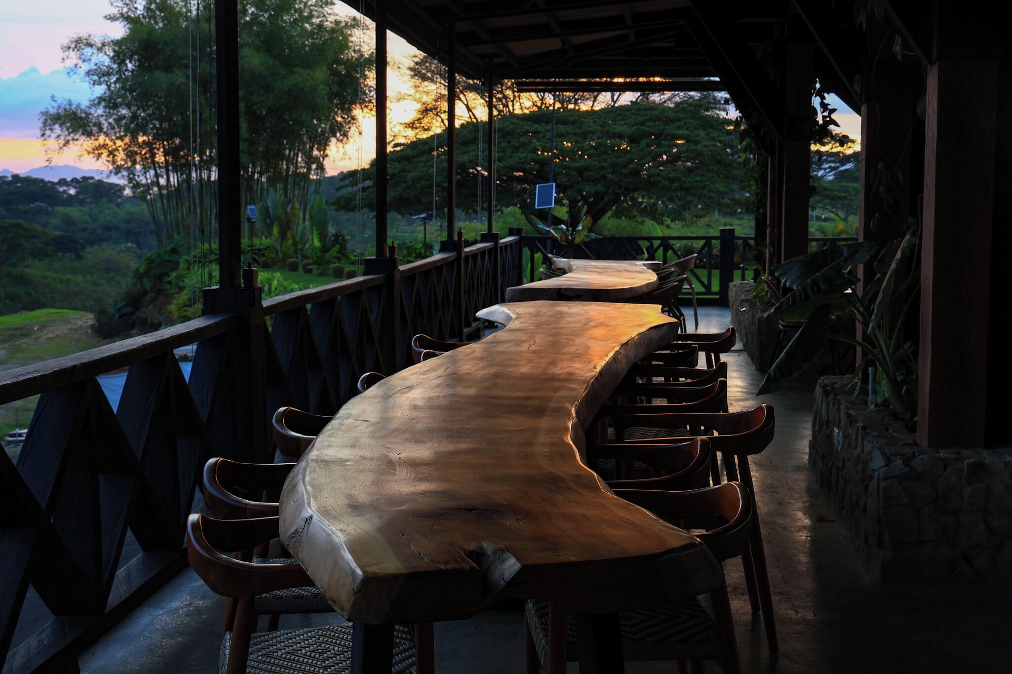 A long wooden table with chairs under a covered area with a view of a lush landscape.