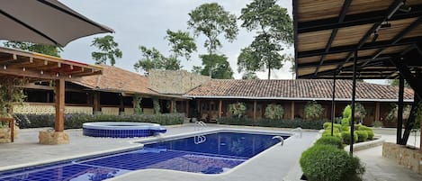A swimming pool with a tiled deck, surrounded by stone walls and covered areas with wooden beams.