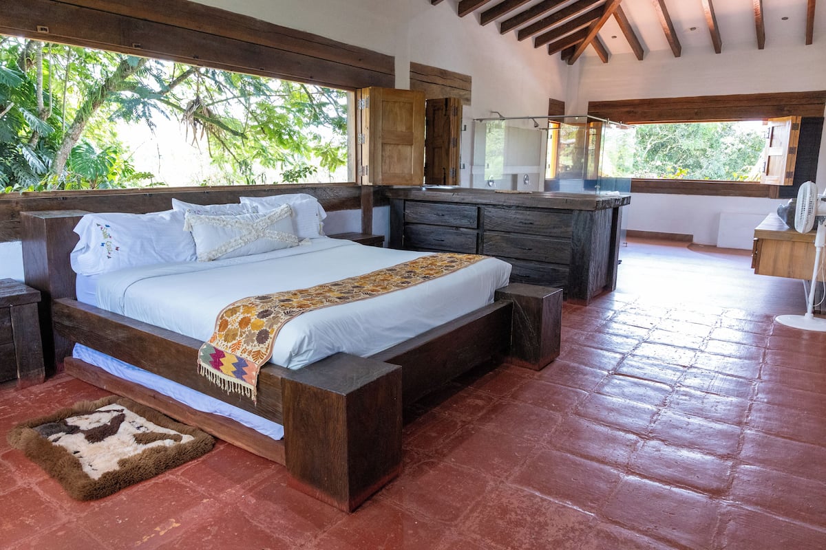 Une chambre spacieuse avec un grand lit, une tête de lit en bois et une vue sur une végétation luxuriante.