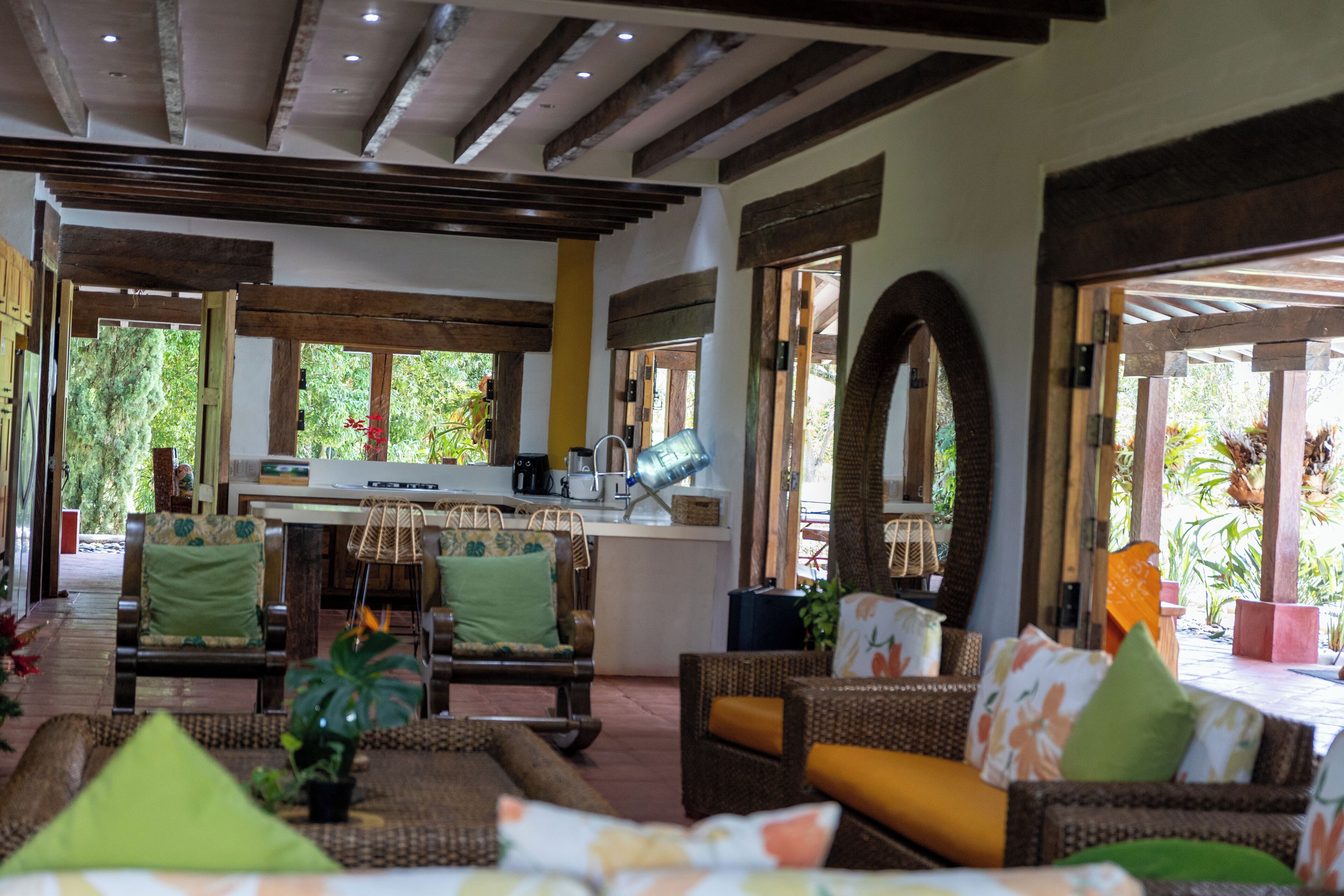 Un vaste espace intérieur aménagé avec des meubles en osier, un coin cuisine et de grandes fenêtres.
