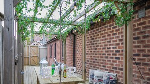 A wooden deck with a picnic table, bottles, glasses, and a lantern. - Experience sociable luxury with all ground floor amenities. (Gloucester)