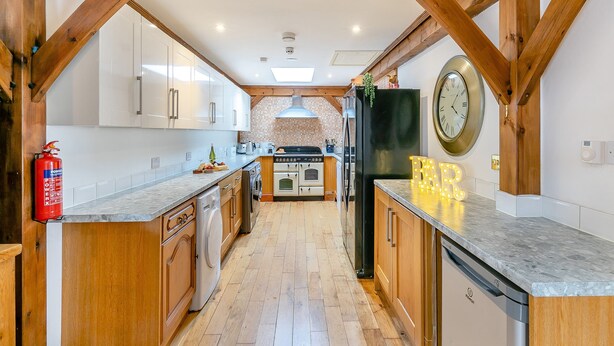 A kitchen with wooden beams, a black refrigerator, and a clock on the wall. - Experience sociable luxury with all ground floor amenities. (Gloucester)