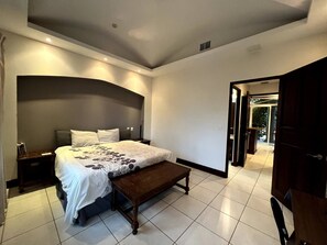 Relax in this serene bedroom with a large bed, two nightstands, and a bench, offering a peaceful retreat with a door to an outdoor area.