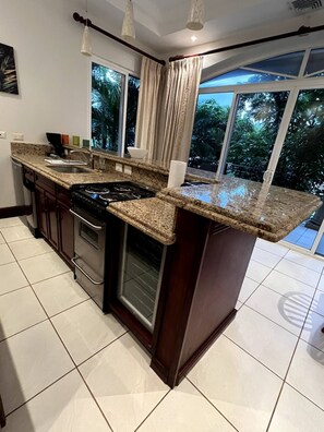 Enjoy cooking in this well-equipped kitchen with a large window offering a view of lush greenery.