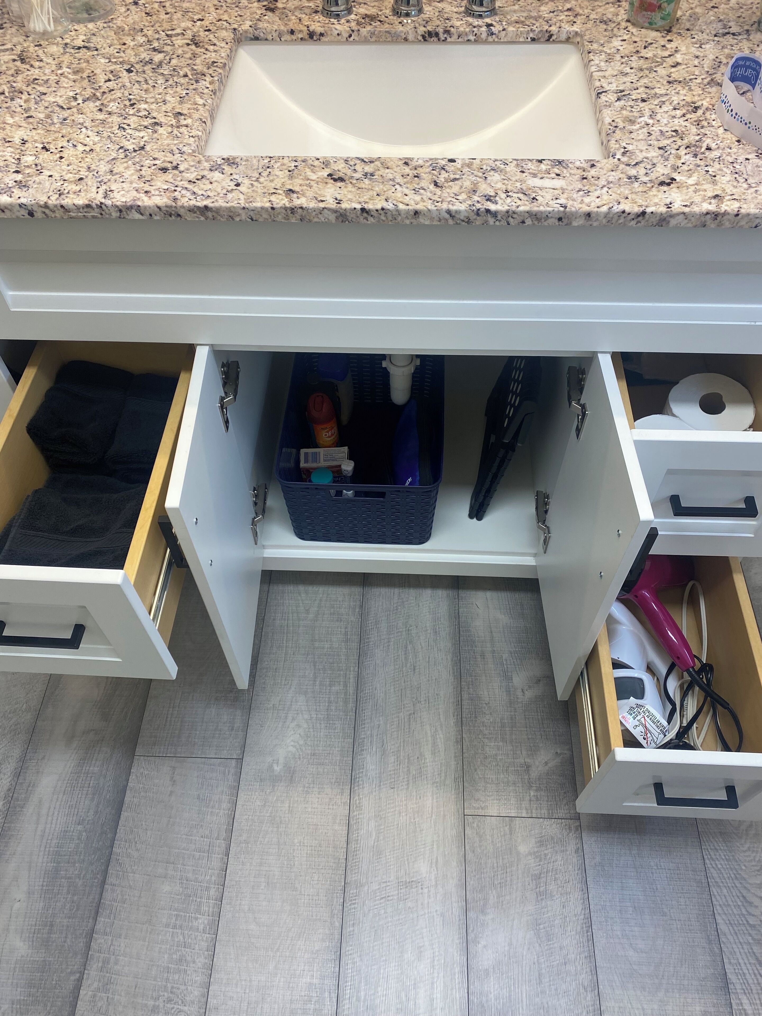 A kitchen with a granite countertop, a white sink, and two open drawers under the sink.