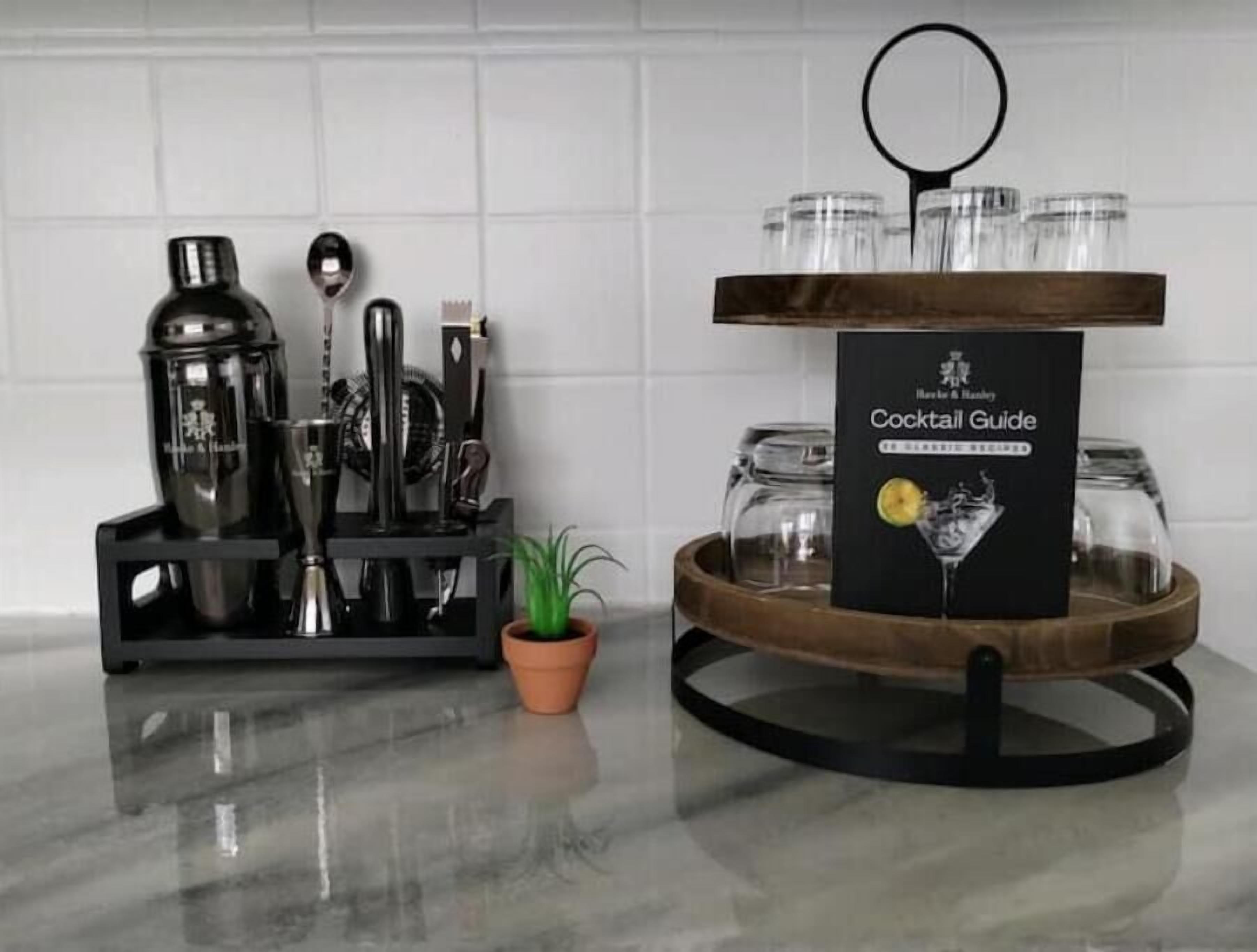 A cocktail station with a guide, a shaker set, a strainer, a jigger, a spoon, and a small potted plant.
